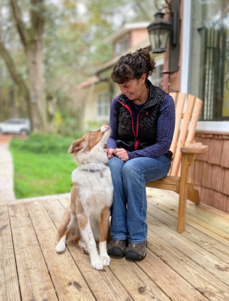 Woman sitting on a wood chair looking down at a dog. The dog is looking up at her admiringly.